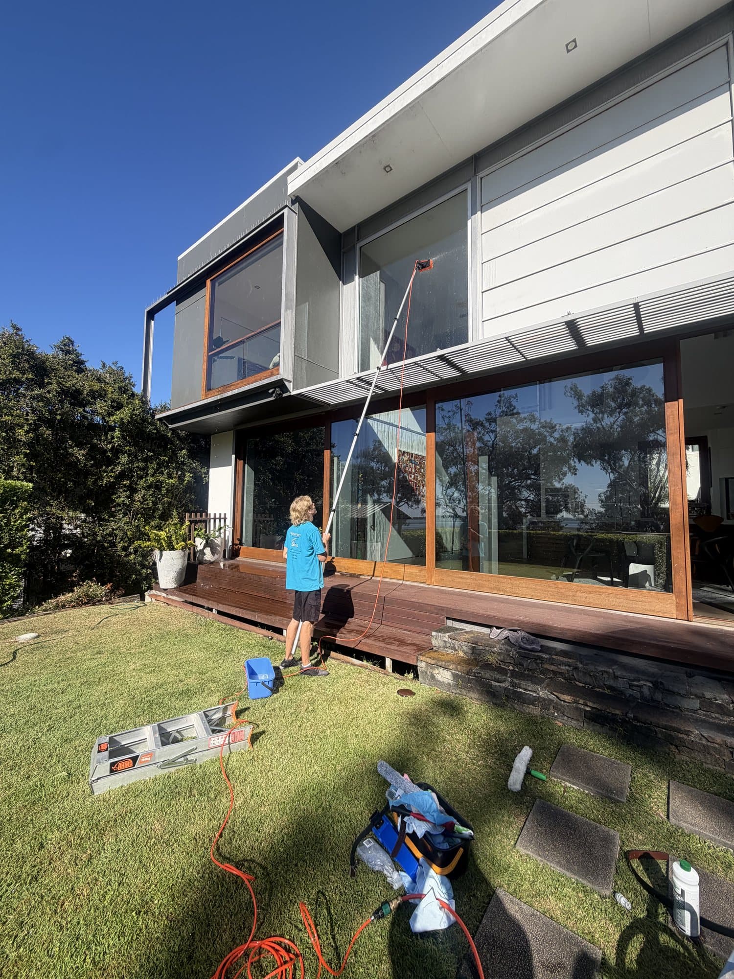 Squeegee Bros cleaning second-storey glass from the lawn with a water-fed pole